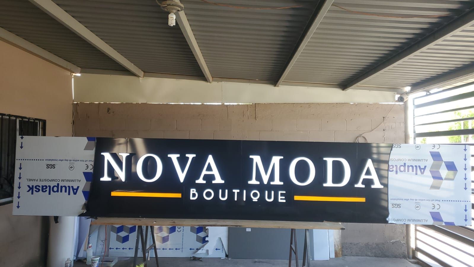 Letras de canal blancas iluminadas de Nova Moda Boutique montadas sobre charola negra, probadas encendidas en el taller.