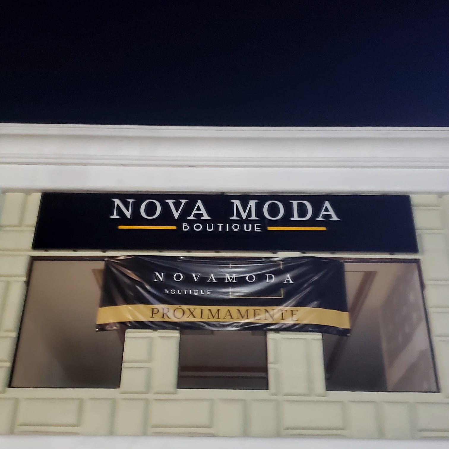 El anuncio de Nova Moda Boutique ya instalado y encendido de noche sobre la fachada del local.
