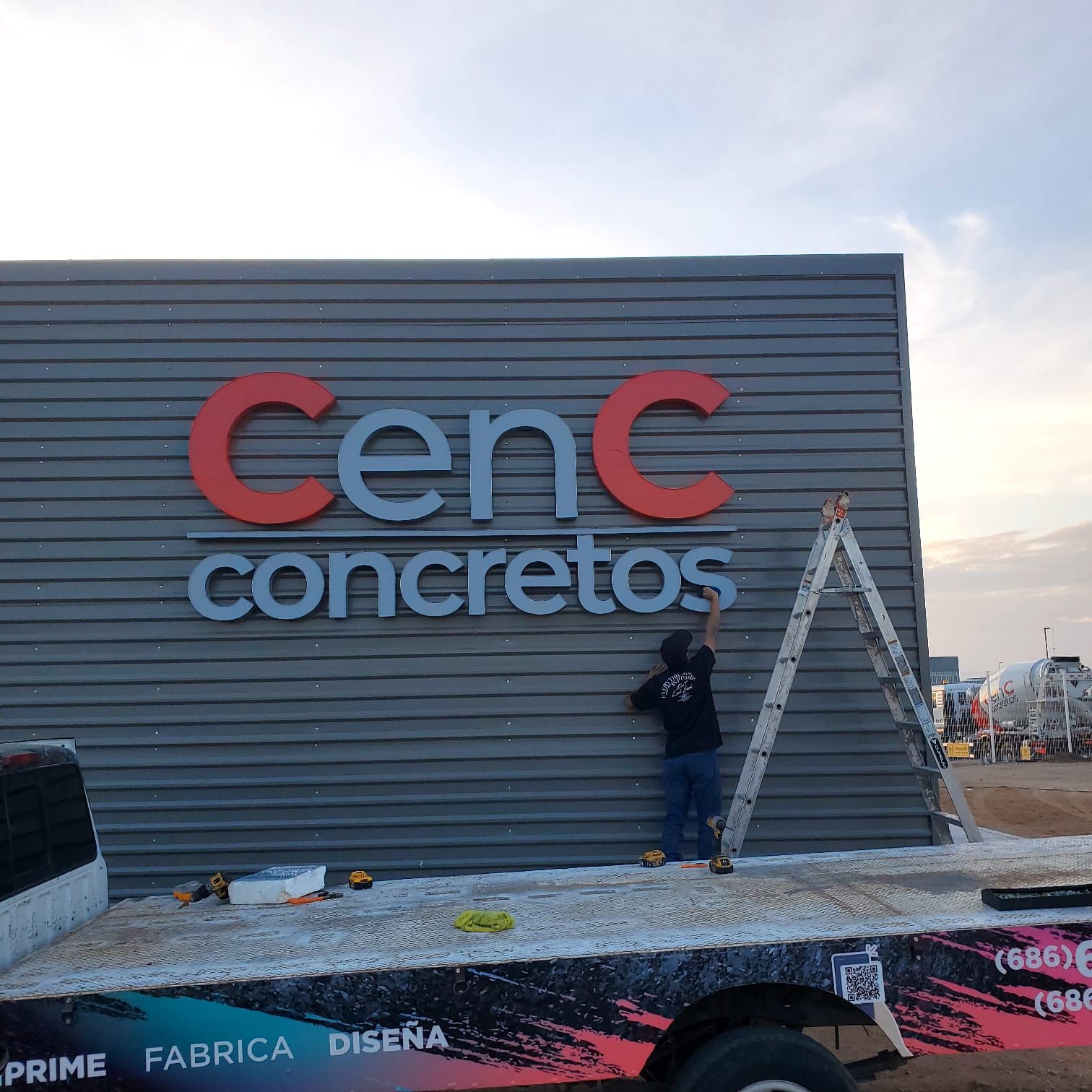 Instalación de las letras de canal de CenC Concretos sobre fachada de lámina acanalada, con el técnico ajustando la última letra desde la plataforma.