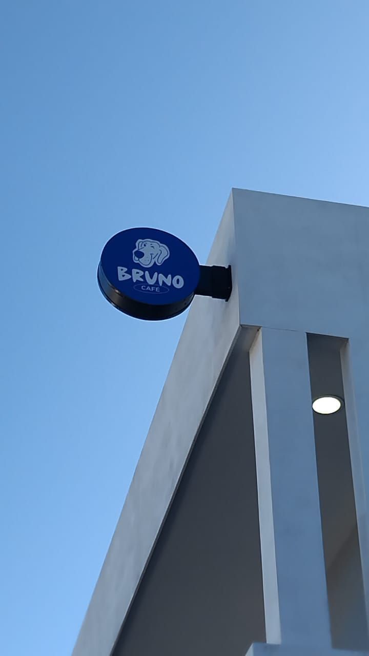 Bandera publicitaria circular de Bruno Café en azul, en voladizo sobre la esquina del edificio contra cielo despejado.