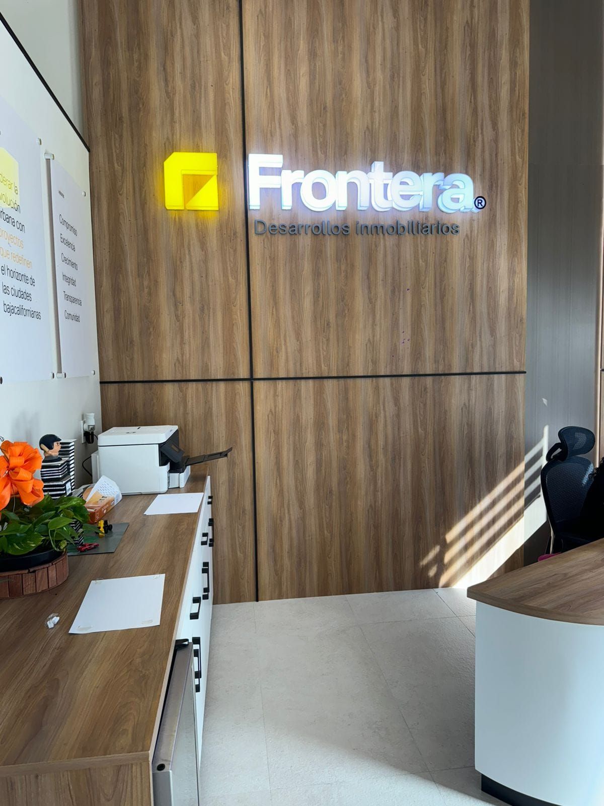 Letras retroiluminadas de Frontera Desarrollos Inmobiliarios sobre muro de madera en la recepción de las oficinas.
