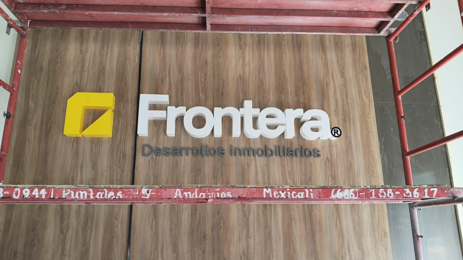 Letras de Frontera montadas sobre panel de aluminio símil madera, fotografiadas desde el andamio durante la instalación.
