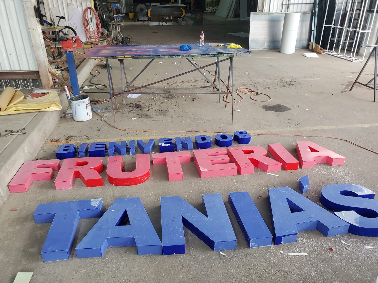 Las letras corpóreas de Tania's Frutería, en azul y rojo, acomodadas en el piso del taller antes del traslado a obra.